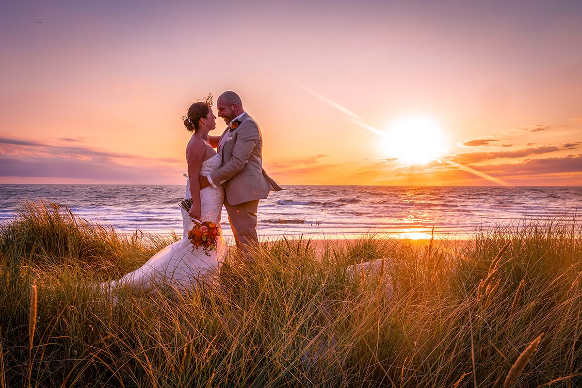 Trouwen op Texel, bruidspaar met zonsondergang in de duinen met de zee op de achtergond