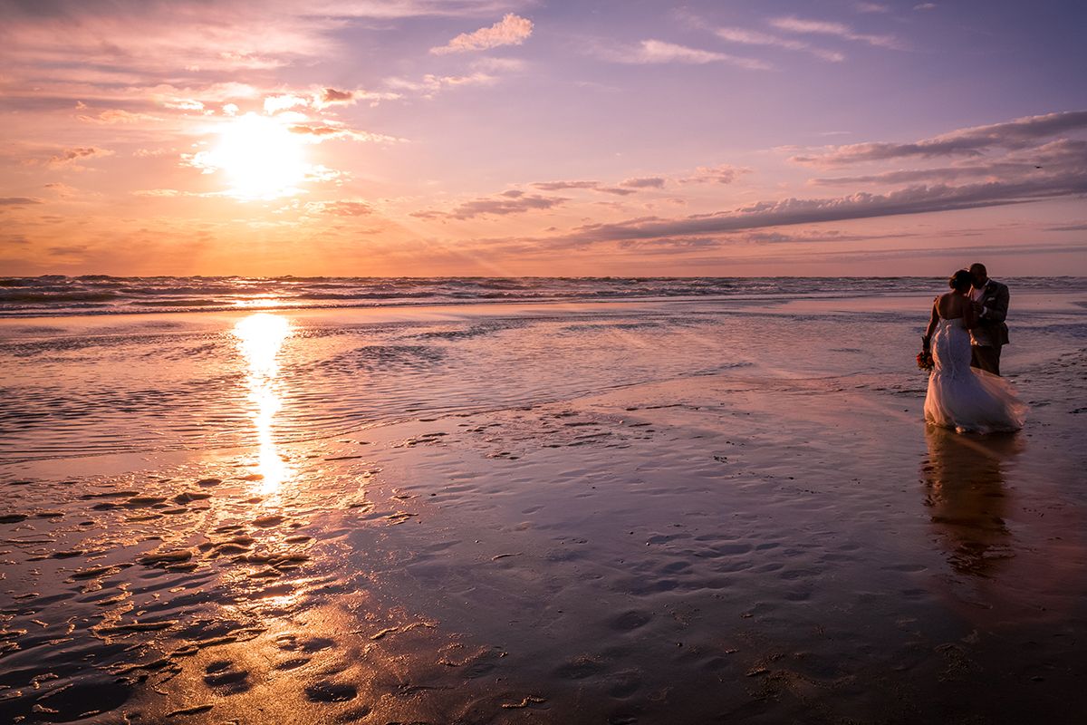 Trouwen op Texel, bruidspaar met zonsondergang in de zee met bruidsjurk!