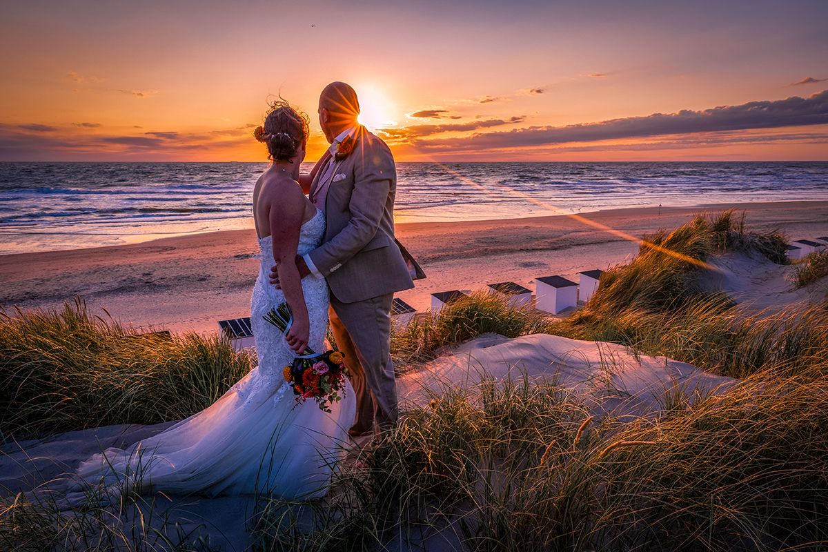 Trouwen op Texel, bruidspaar met zonsondergang in de duinen met de zee op de achtergond